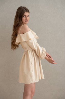 Güzel, genç, gülümseyen bir kadın portresi. Dalgalı saçlı. İç kısımda bej bir elbise giymiş. 