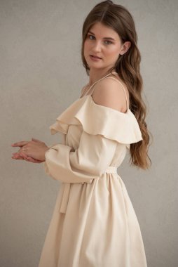 Güzel, genç, gülümseyen bir kadın portresi. Dalgalı saçlı. İç kısımda bej bir elbise giymiş. 