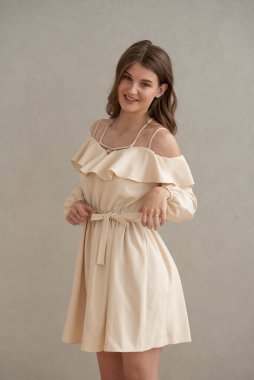 Güzel, genç, gülümseyen bir kadın portresi. Dalgalı saçlı. İç kısımda bej bir elbise giymiş. 