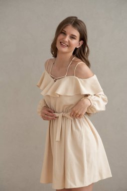 Güzel, genç, gülümseyen bir kadın portresi. Dalgalı saçlı. İç kısımda bej bir elbise giymiş. 