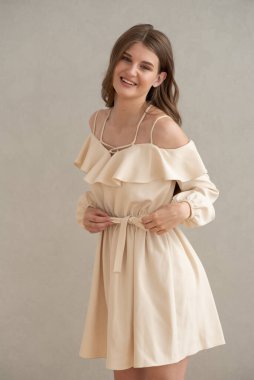 Güzel, genç, gülümseyen bir kadın portresi. Dalgalı saçlı. İç kısımda bej bir elbise giymiş. 