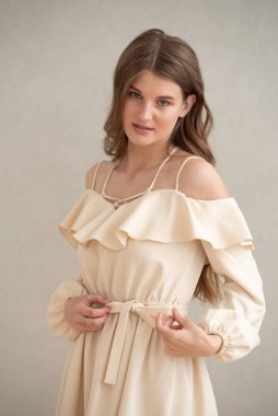 Güzel, genç, gülümseyen bir kadın portresi. Dalgalı saçlı. İç kısımda bej bir elbise giymiş. 