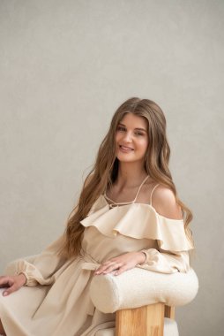 Güzel, genç, gülümseyen bir kadın portresi. Dalgalı saçlı. İç kısımda bej bir elbise giymiş. 