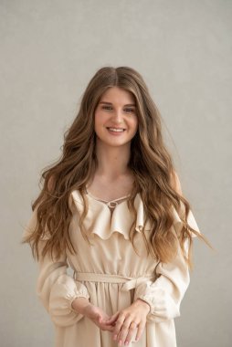 Güzel, genç, gülümseyen bir kadın portresi. Dalgalı saçlı. İç kısımda bej bir elbise giymiş. 