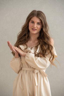 Güzel, genç, gülümseyen bir kadın portresi. Dalgalı saçlı. İç kısımda bej bir elbise giymiş. 