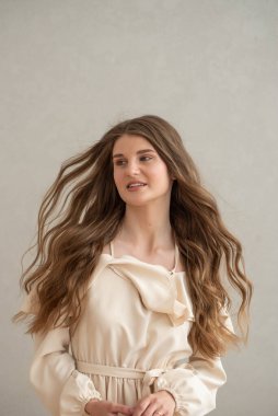 Güzel, genç, gülümseyen bir kadın portresi. Dalgalı saçlı. İç kısımda bej bir elbise giymiş. 