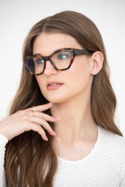 Görme yeteneğini geliştirmek için gözlük takan güzel bir genç kadın portresi. Güzel dalgalı saçlar, gündüz makyajı, parlak bir iç mekanda normal kıyafetler.