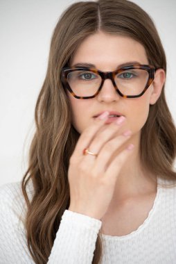 Görme yeteneğini geliştirmek için gözlük takan güzel bir genç kadın portresi. Güzel dalgalı saçlar, gündüz makyajı, parlak bir iç mekanda normal kıyafetler.