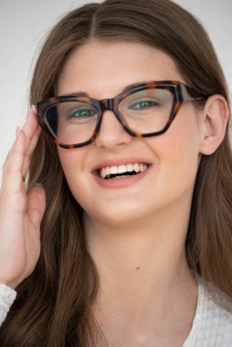 Görme yeteneğini geliştirmek için gözlük takan güzel bir genç kadın portresi. Güzel dalgalı saçlar, gündüz makyajı, parlak bir iç mekanda normal kıyafetler.