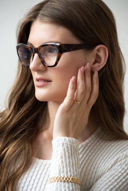 Görme yeteneğini geliştirmek için gözlük takan güzel bir genç kadın portresi. Güzel dalgalı saçlar, gündüz makyajı, parlak bir iç mekanda normal kıyafetler.