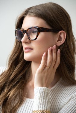 Görme yeteneğini geliştirmek için gözlük takan güzel bir genç kadın portresi. Güzel dalgalı saçlar, gündüz makyajı, parlak bir iç mekanda normal kıyafetler.