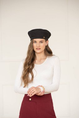 Güzel bir genç kız klasik şort, beyaz bir kazak, kafasında bere ve parlak bir iç mekanda mokasen giyiyor.