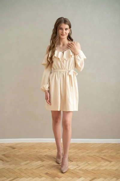 stock image Beautiful young smiling woman portrait with wavy hair, dressed in a beige dress posing in the interior 