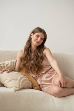 Beyaz arka planda rahat iç çamaşırlarıyla gülümseyen ve başka tarafa bakan kendine güvenen güzel bir genç kadın..