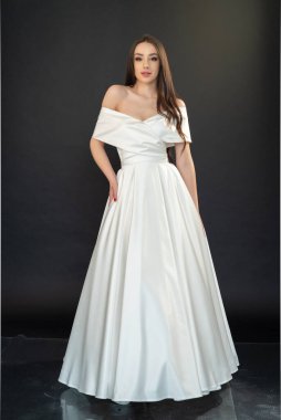 Gri arka planda poz veren beyaz gelinlikli güzel bir kadın. 