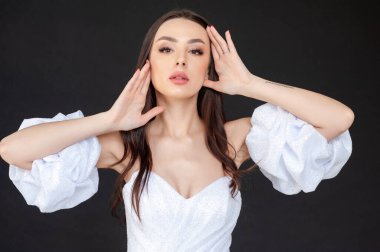 Gri elbiseli ve beyaz elbiseli genç kadın, gri renkte yalnız poz veriyor. 