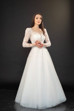 Gelinlik giymiş, gri bir arka planda duran güzel bir kızın tam boy portresi. 