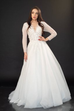 Gri stüdyo arka planında poz veren beyaz gelinlikli güzel esmer kadın. 