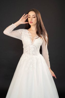 Gri arka planda uzun saçlı güzel bir kadın gelinlik giyiyor. 