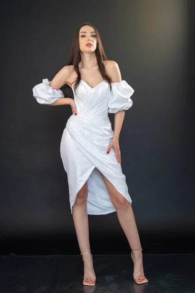 stock image portrait of a beautiful woman with long wavy hair posing in white dress on gray background. 