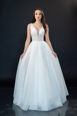 Gri arka planda güzel bir gelinlik ve lüks beyaz gelinlik içinde genç bir gelin..