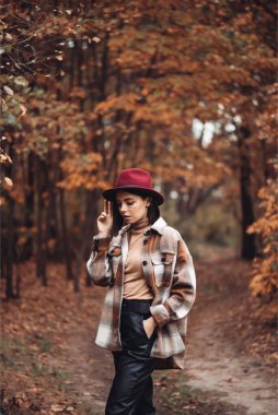 Sonbahar ormanında şapkalı ve ceketli genç bir kız. 