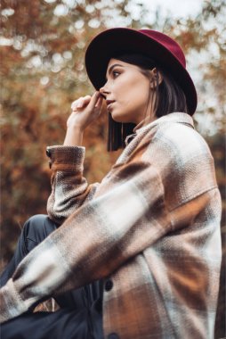 Genç bir kadın bankta oturuyor ve başka tarafa bakıyor. 