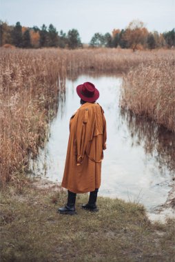 Siyah paltolu ve şapkalı genç bir adam ormanda bir tarlada yürüyor. 