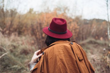 Sonbaharda, sonbahar parkında, şapkalı genç bir kız yürüyor. 