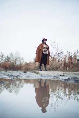 Siyah ceketli genç bir adam ve arkasında sırt çantası olan bir şapka.