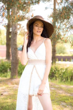 Yazlık beyaz şapkalı güzel esmer kadın güneşli bir günde parkta poz veriyor.. 