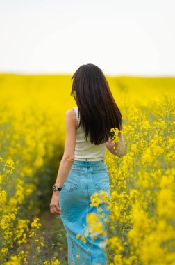 Sarı elbiseli ve kot pantolonlu genç bir kız elinde bir buket çiçekle ayakta duruyor.. 