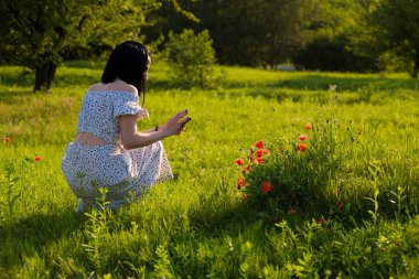 Yeşil çimenlerde oturan ve akıllı telefona bakan bir kadın.