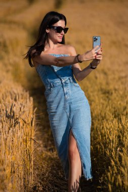 Buğday tarlasında genç bir kız. Genç bir kız tarlaların ortasında akıllı telefonuyla fotoğraf çekiyor.