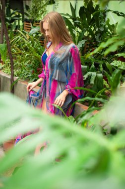  Renkli bir elbiseyle bahçede yürüyen bir kadın.