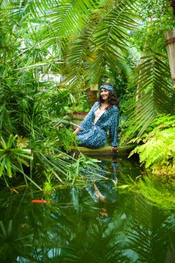 Nehrin yeşil yapraklarında mavi elbiseli ve şapkalı kadın..