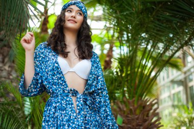 Genç, güzel, kumsalda poz veren mavi mayolu esmer kadın.