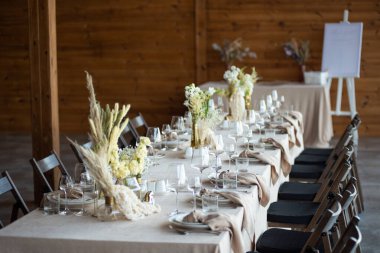 Düğünde ya da akşam yemeğinde ahşap masada çiçekler ve çatal bıçaklarla güzel bir masa.