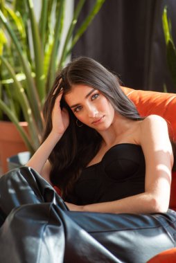 Güzel esmer kız iç kısımdaki koltukta siyah deri ceketli poz veriyor.