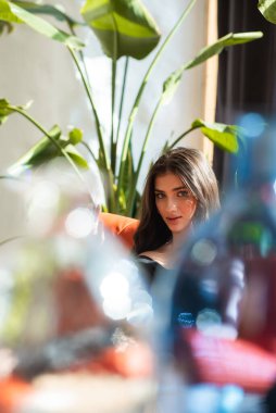 Siyah elbiseli genç bir kadın elinde çiçeklerle yerde oturuyor ve kameraya bakıyor.