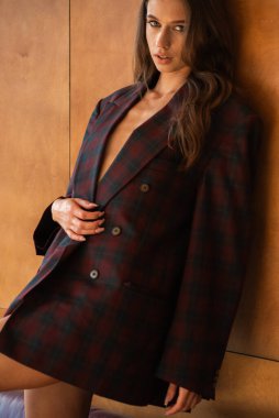 Kırmızı ceketli ve kareli gömlekli genç seksi kadın evde poz veriyor.