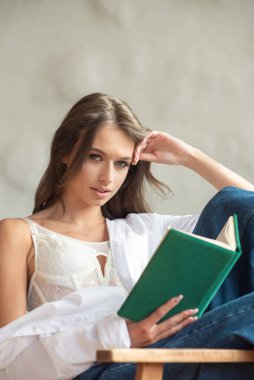 Kitaplı genç bir kız bankta oturuyor.
