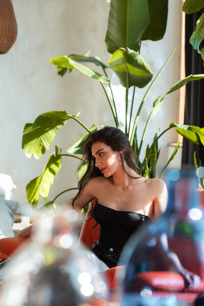 portrait of beautiful brunette woman with dark hair in black dress posing in interior with green plants.