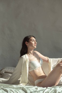 Beyaz iç çamaşırlı güzel bir kadın sabahları evde yatağında oturuyor.