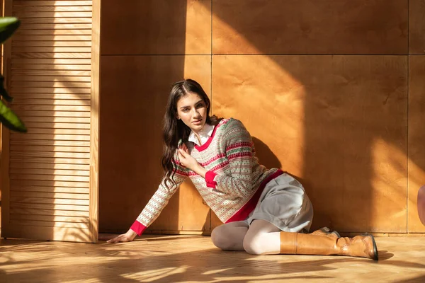 beautiful young woman in a sweater and a knitted sweater on a background of a wooden window with a wooden floor