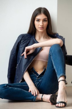 Beyaz arka planda kot pantolon ve ceket giyen genç bir kadın.