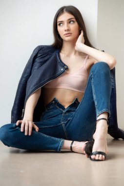 Beyaz arka planda kot pantolon ve ceket giyen genç bir kadın.