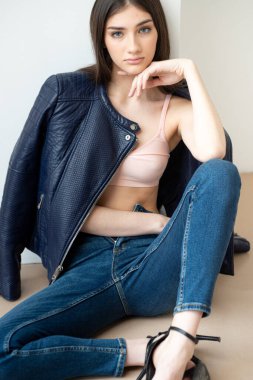 Beyaz arka planda kot pantolon ve ceket giyen genç bir kadın.