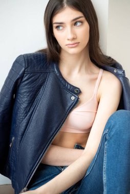 Beyaz arka planda kot pantolon ve ceket giyen genç bir kadın.