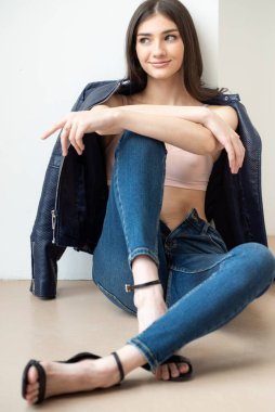 Beyaz arka planda kot pantolon ve ceket giyen genç bir kadın.